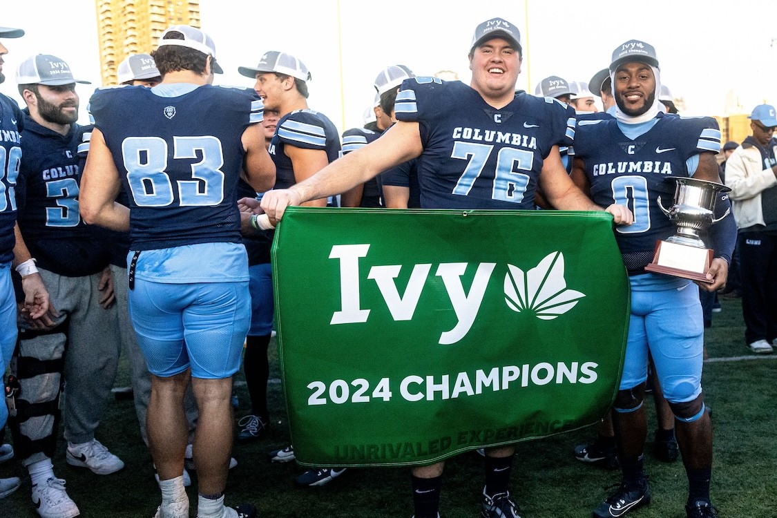 Two Columbia University football players holding a green flag that reads "Ivy 2024 Champions"