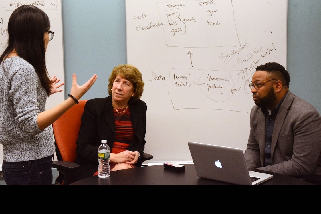 Kathy McKeown and Desmond Patton sitting at a table and listening to a student.