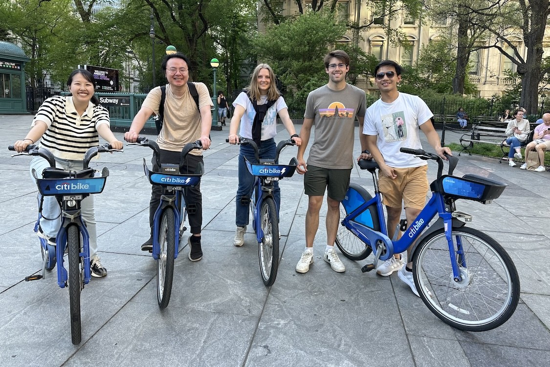 Five people smiling for a photo. Four of them are mounted on Citi bikes.