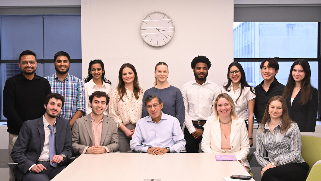 Asheet Mehta and Columbia Engineering students pose for a photo in a conference room arranged in two rows behind a meeting table