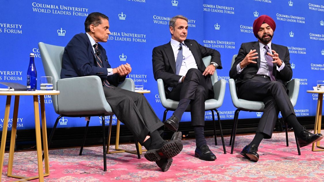 Fareed Zakaria looking toward Kyriakos Mitsotakis and Ajay Banga, who is speaking, during a panel discussion at the Columbia University World Leaders Forum.