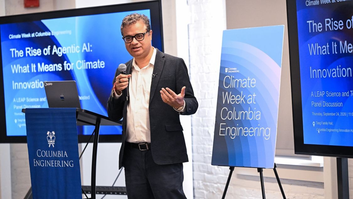 Vishal Misra speaks into a microphone beside displays for a Climate Week at Columbia Engineering panel on agentic AI and climate innovation.