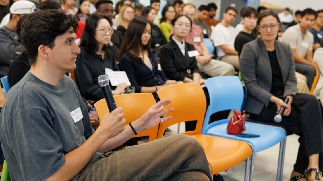 Student asks a question into a microphone as audience members look toward him.