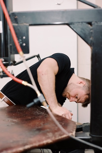 A person works intently at a machine holding wood