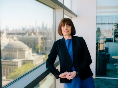Gordana Vunjak-Novakovic smiling near a window, with a university campus and city skyline in the background