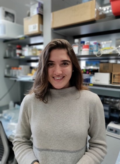 Ilaria Baldassarri smiling in a research lab, with lab shelves holding bottles, boxes, and equipment in the background