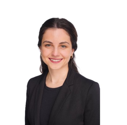 Headshot of Melina Tourni smiling in a black blazer with gold hoop earrings, against a white background.